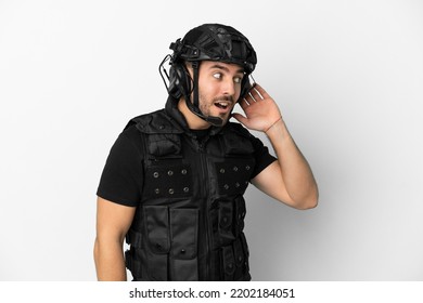 Young Caucasian Swat Isolated On White Background Listening To Something By Putting Hand On The Ear