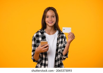 Young caucasian teenage girl pupil student using smart phone for e-banking online, paying with credit card for shopping, new clothes, presents, loan isolated in yellow background.