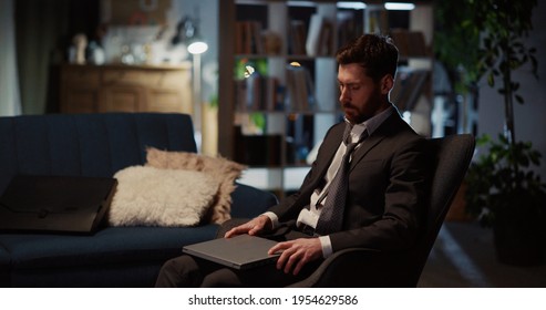 Young Caucasian Tired Arriving Home Returning From Office Late At Night. Unhappy Exhausted Businessman Opening Laptop To Finish Project Before Deadline.