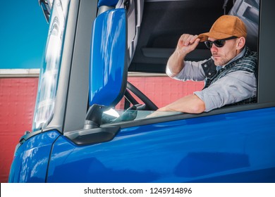 Young Caucasian Truck Driver Wearing Baseball Hat Inside Semi Cabin.