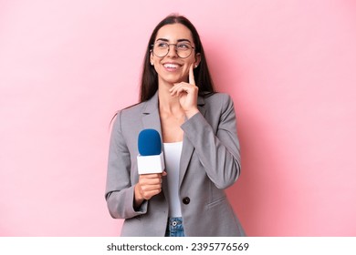Young caucasian tv presenter woman isolated on pink background thinking an idea while looking up