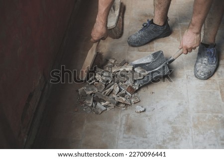 Young caucasian unrecognizable man sweeping construction debris with a small whisk on an old dustpan from a dirty tiled floor, close-up . The concept of cleaning and installing windows, construction w