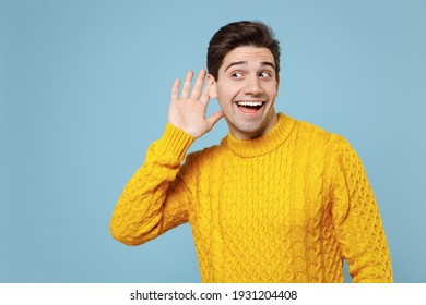 Young Caucasian Unshaved Curious Fun Student Man 20s Wear Casual Knitted Cozy Yellow Fashionable Sweater Try To Hear You Overhear Listening Intently Isolated On Blue Color Background Studio Portrait.