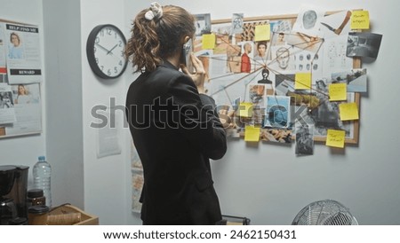 Young caucasian woman analyses evidence on a cork board at a police station while on the phone