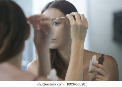 Young Caucasian Woman Applying Serum For Eyebrows And Eyelashes Growth In Front Of The Mirror. Night Time Beauty Routine.	