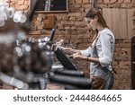 Young caucasian woman in apron working with cash box in coffee shop behind the counter. Female worker, barista, waitress, manager, administrator checking bill order on digital cash register.
