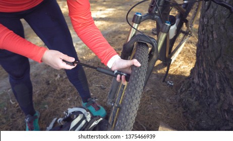 Young caucasian woman athlete tourist cyclist uses a hand tool, a bicycle pump to inflate air into a tire wheel mountain bike. Breakdown and quick repair of a bicycle in the countryside outside. - Powered by Shutterstock