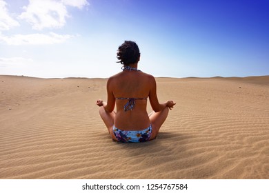 Young Caucasian Woman In A Biking Is Doing Yoga Exercises In The Dunes Of Maspalomas, Gran Canaria