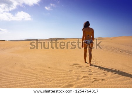 Young caucasian woman in a biking is walking along the dunes of Maspalomas, Gran Canaria