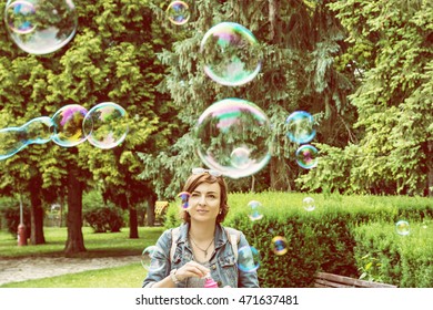 Young Caucasian Woman Blowing Soap Bubbles In The City Park. Leisure Activity. Natural Beauty. Outdoor Activity. Warm Photo Filter. Summer Holiday.