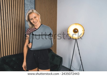 Young Caucasian woman with broken arm and wearing a sling at home and smiling, medium shot. High quality photo