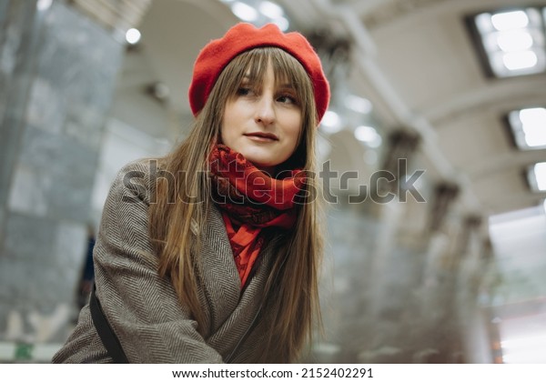 young caucasian woman with brown hair wearing elegant\
classy coat and a scarf sitting alone in subway carriage and\
distantly looking out window. Image with selective focus, toning\
and noise effect. 