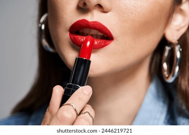 A young Caucasian woman with brunette hair applying bright red lipstick to her lips in a studio setting. - Powered by Shutterstock