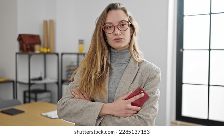 Young caucasian woman business worker holding smartphone standing with arms crossed gesture and serious expression at office - Powered by Shutterstock