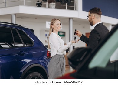 Young caucasian woman buys a car at a car dealership. Bearded man seller gives the car keys - Powered by Shutterstock