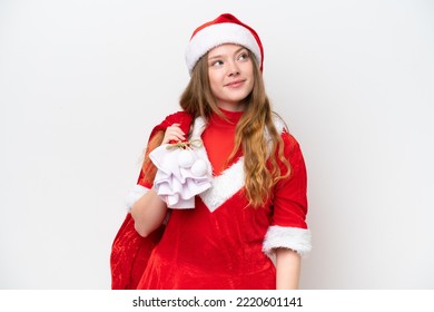 Young Caucasian Woman With Christmas Dress Holding Christmas Sack Isolated On White Background Looking Up While Smiling