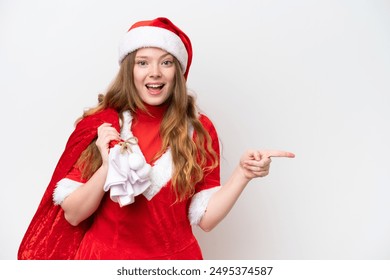 Young caucasian woman with Christmas dress holding Christmas sack isolated on white background surprised and pointing finger to the side - Powered by Shutterstock