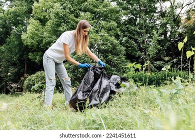 Young caucasian woman cleaning-up public park or forest of plastic garbage. Volunteer picking up plastic bottle in woods. Green and clean nature, avoid pollution, be friendly to the environment and - Powered by Shutterstock