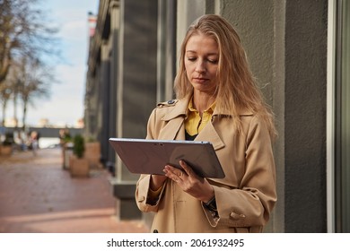 Young Caucasian Woman In Coat Using Tablet Outdoors On Sunny Day, Reading Ebook, Watching Movie. Attractive Female Street Portrait At Fall Or Spring. Autumn Lifestyle, Modern Communication Technology