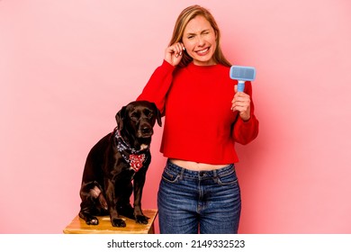 Young Caucasian Woman Combing The Dog Isolated On Pink Background Covering Ears With Hands.