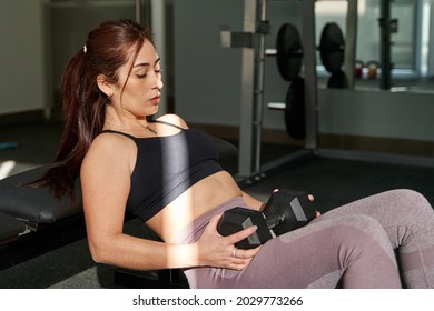 young caucasian woman concentrating on performing hip thrust with a dumbbell alone in gymnasium