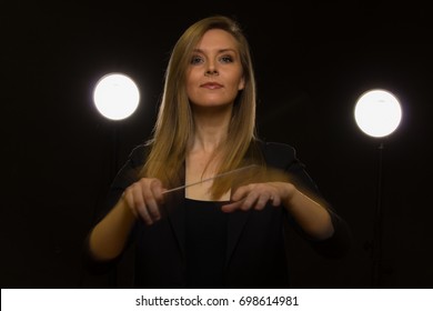 Young Caucasian Woman Conductor Poses With Baton In A Dark Space With Stage Lights