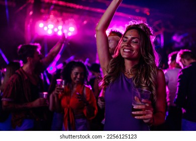 A young Caucasian woman is dancing at a concert having a good time at an open air venue in the night.