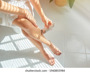 Young Caucasian Woman Depilates Her Leg With An Electric Epilator Device In The Bathroom.