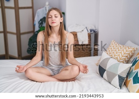 Young caucasian woman doing yoga exercise sitting on bed at bedroom
