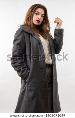 Young Caucasian woman and dressed in gray coat posing in studio, isolated on white background
