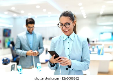 Young Caucasian Woman Dressed In Suit Trying Out New Smart Phone. Tech Store Interior.