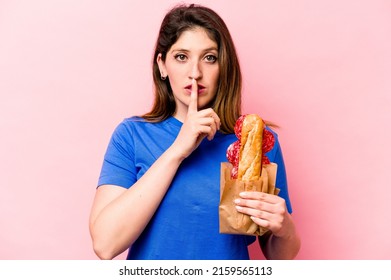 Young Caucasian Woman Eating A Sandwich Isolated On Pink Background Keeping A Secret Or Asking For Silence.