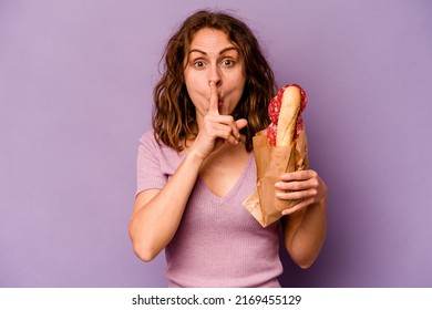 Young Caucasian Woman Eating A Sandwich Isolated On Purple Background Keeping A Secret Or Asking For Silence.