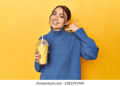 Young caucasian woman enjoying a creamy vanilla shake showing a mobile phone call gesture with fingers. - Powered by Shutterstock