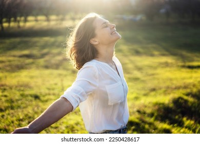 Young caucasian woman enjoying the sun and summer in a green field in the rays of the sun with her arms wide open - Powered by Shutterstock