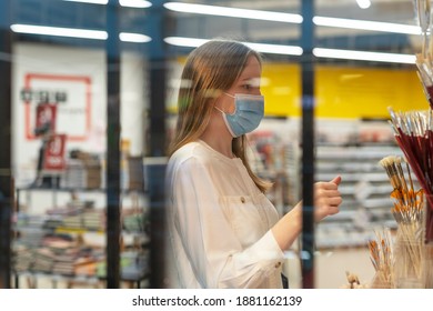 Young caucasian woman in face mask in shop choosing brushes through window.