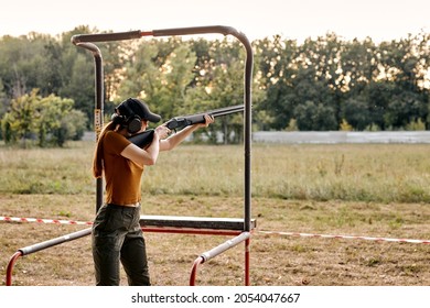 young caucasian woman in goggles and headset aiming rifle at side, ready to shoot in an outdoor range. Skilled experienced female side view. Firearms for sports shooting, hobby.