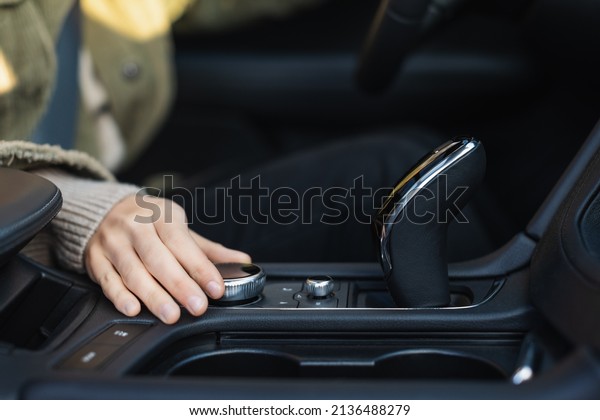 Young\
caucasian woman hand\'s turns the control wheel of a modern\
multimedia system in the car. Vehicle interior. Adding volume.\
Freedom of movement concept. Selective\
focus.