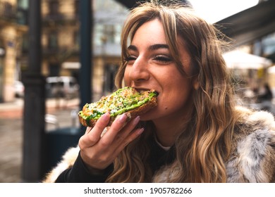 Young caucasian woman having breakfast at a terrace eating an avocado toast.