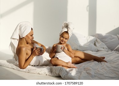 A Young Caucasian Woman With His Daughter On A Bed At Home In The Morning, Wearing In Towel Play And Drink A Milk