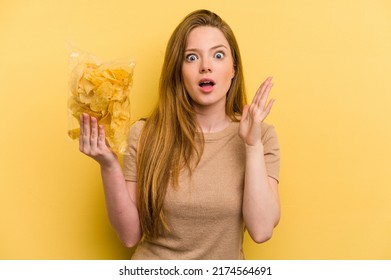 Young Caucasian Woman Holding A Bag Of Chips Isolated On Yellow Background Surprised And Shocked.