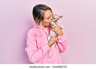 Young caucasian woman holding beautiful small chihuahua dog hugging and kissing pet with love