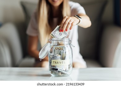 Young Caucasian Woman Holding Big Glass Bottle With Cash Money Dollar Bill On White Marble Table At Home. Saving Money For Future Travel Concept.