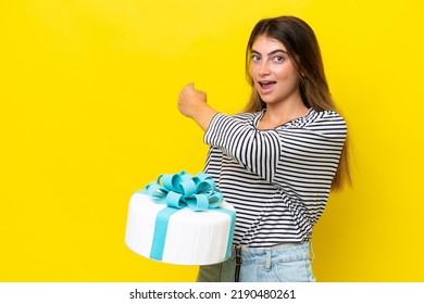 Young Caucasian Woman Holding Birthday Cake Isolated On Yellow Background Pointing Back