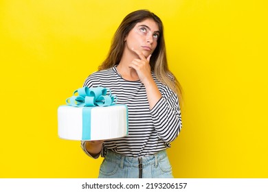 Young Caucasian Woman Holding Birthday Cake Isolated On Yellow Background Having Doubts