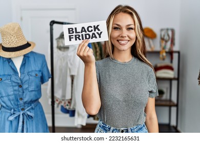 Young caucasian woman holding black friday banner at retail shop looking positive and happy standing and smiling with a confident smile showing teeth  - Shutterstock ID 2232165631