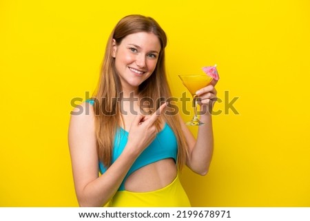 Young caucasian woman holding a cocktail isolated on yellow background and pointing it