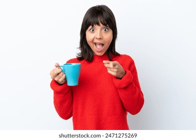 Young caucasian woman holding cup of coffee isolated on white background surprised and pointing front - Powered by Shutterstock