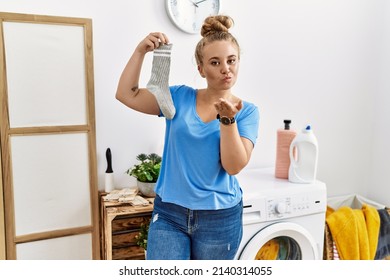 Young Caucasian Woman Holding Dirty Sock At Laundry Room Looking At The Camera Blowing A Kiss With Hand On Air Being Lovely And Sexy. Love Expression. 