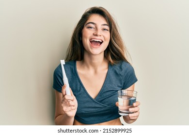 Young caucasian woman holding electric toothbrush and water glass smiling and laughing hard out loud because funny crazy joke.  - Powered by Shutterstock